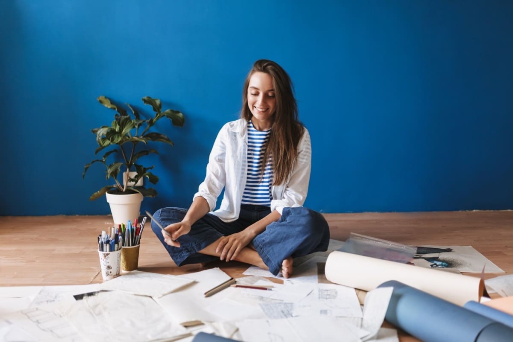 young-smiling-painter-sitting-floor-with-drawings-near-blue-background-home (1).jpg